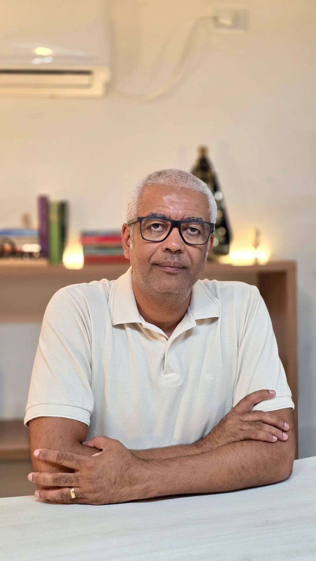 Professor Adriano sentado à mesa, de braços cruzados